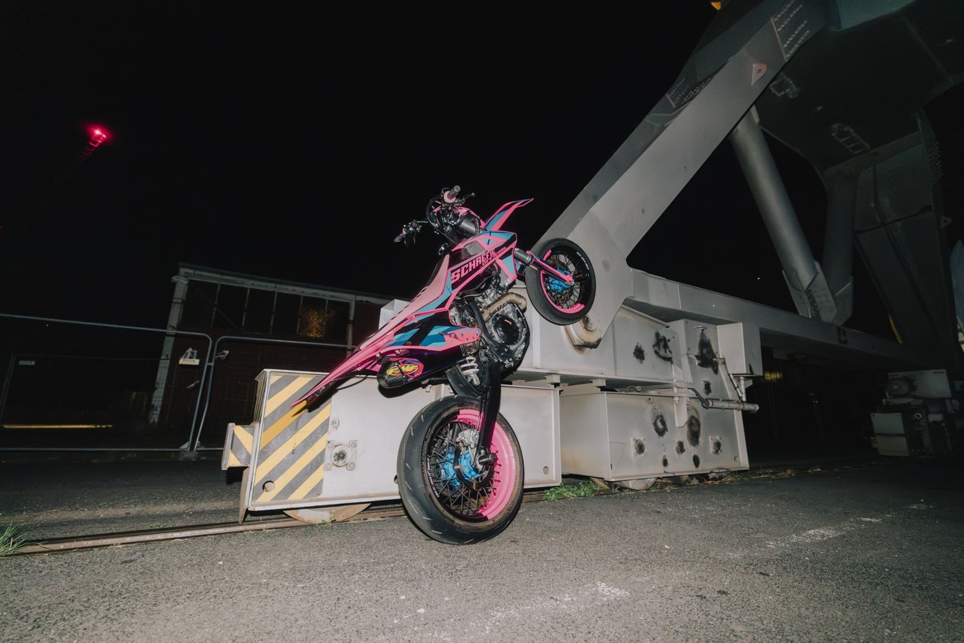 Pinke KTM Supermoto bei Nacht im Hafen, das Vorderrad steht auf dem Boden, das Heck ragt in die Luft